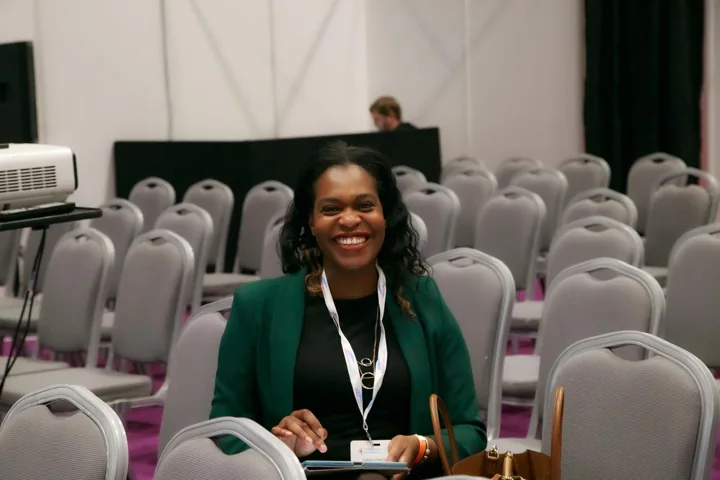 Emma smiling while seated among conference chairs.