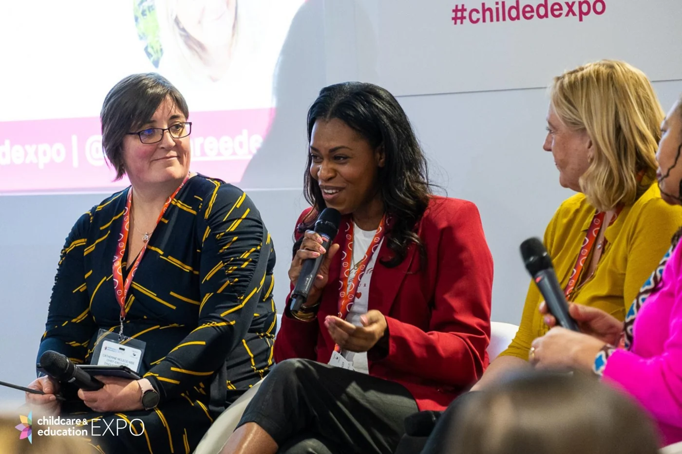 Emma speaking into a microphone during a panel discussion, wearing a red jacket.