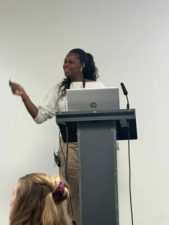 Emma gesturing towards an audience while standing at a lectern.